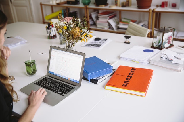 A laptop on a desk with two note books. One is orange, one is blue. 